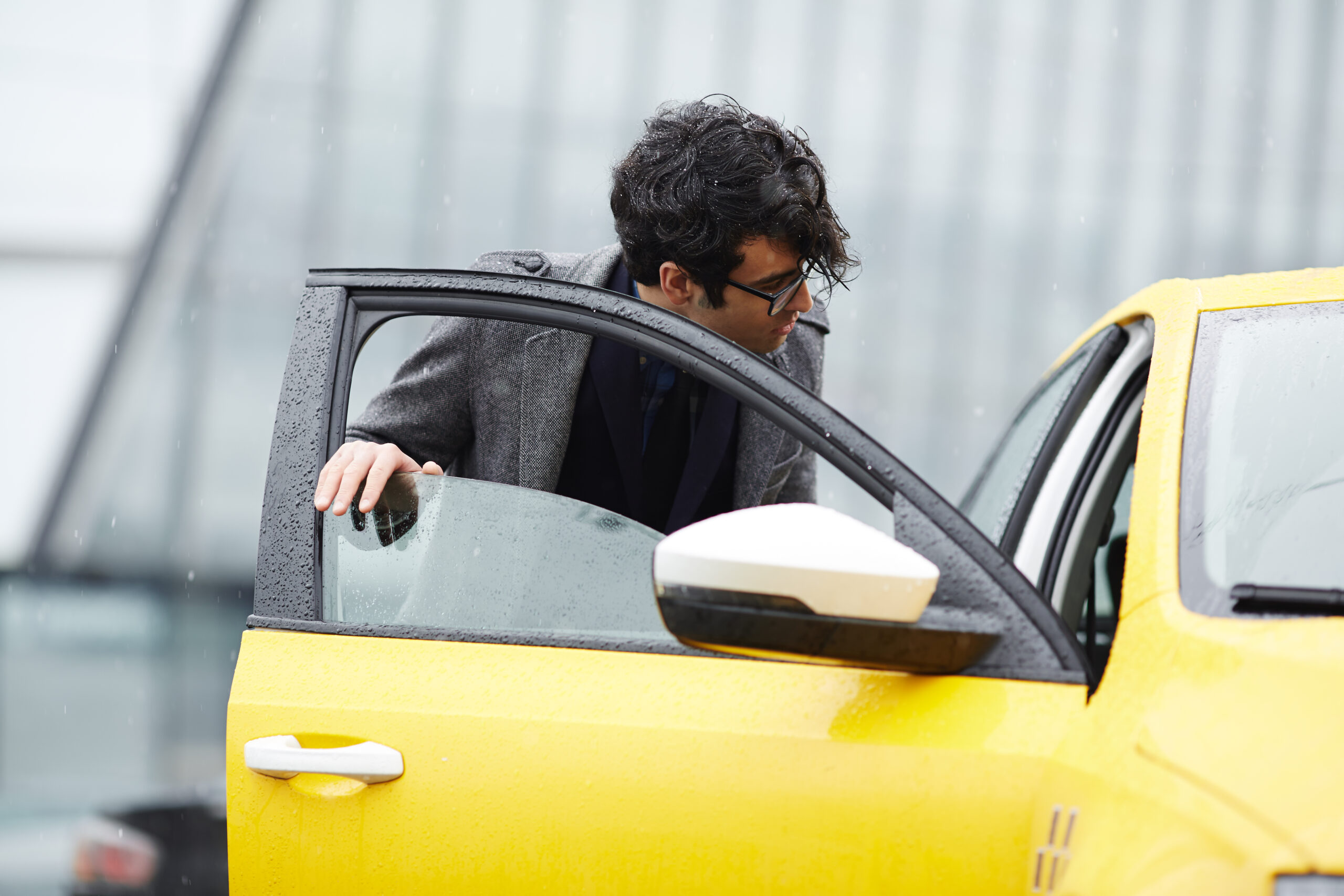 Portrait of hurrying businessman catching taxi and opening car door on rainy autumn street